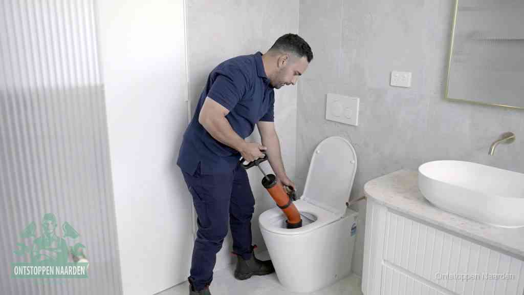 Een monteur buigt over een wandcloset en duwt met de hand een persluchtontstopper in de toiletpot om de verstopping handmatig los te maken in Naarden