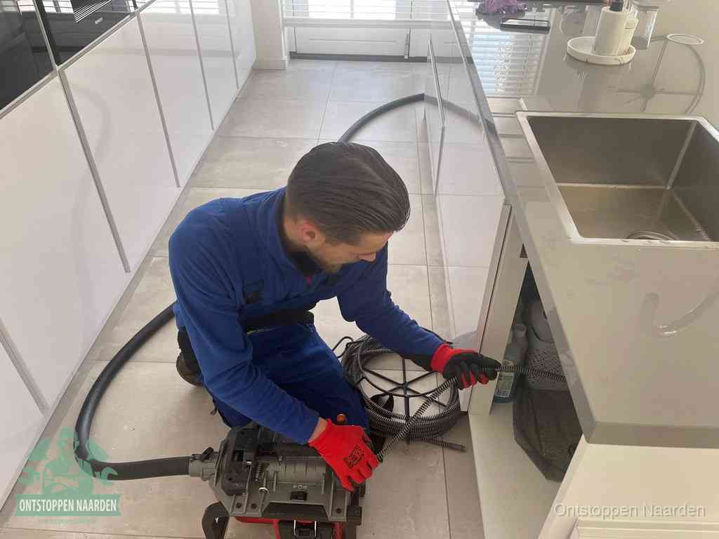 Een monteur ontstopt de keukenafvoer onder de spoelbak met een elektrische veermachine in Naarden
