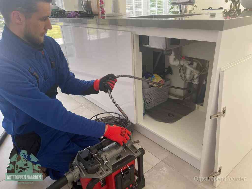 Monteur voert een ontstoppingsveer in de afvoer onder de keuken in Naarden