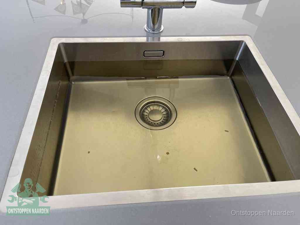Stilstaand water in een rvs spoelbak dat niet wegloopt, een duidelijk signaal van een gootsteenverstopping in Naarden