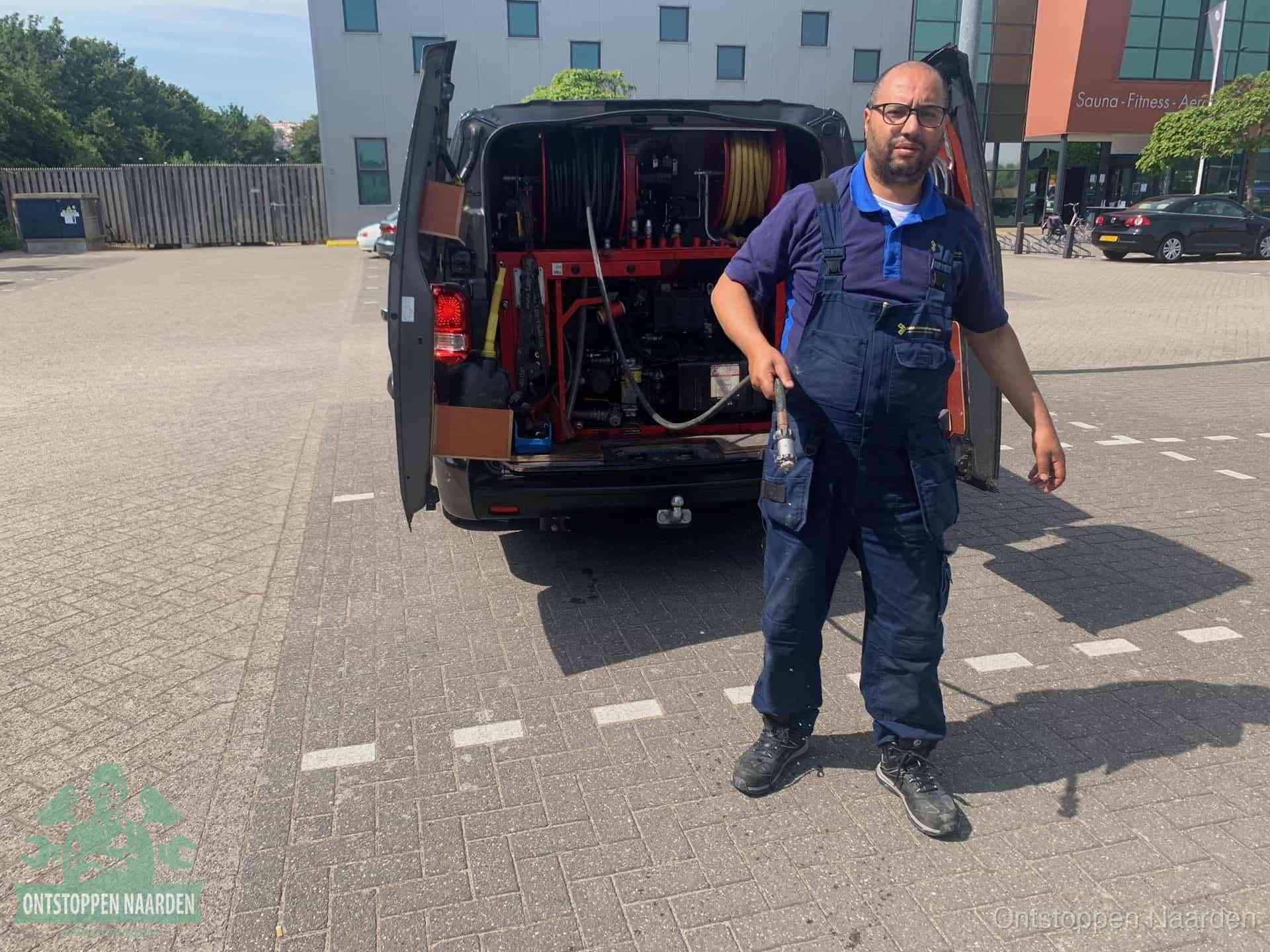 Een monteur bij zijn bestelbus met een hogedruk- en rioolreinigingsunit, klaar om de oorzaak van terugkerende wc-verstoppingen aan te pakken in Naarden