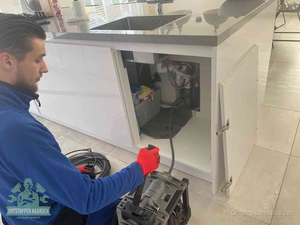 Monteur ontstopt met een veermachine een verstopte afvoer onder de gootsteen in Naarden