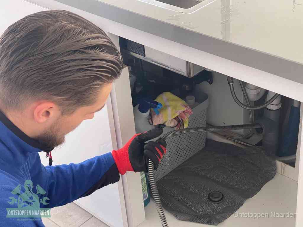Een monteur voert een flexibele ontstoppingsveer in de afvoer om een verstopping voorbij de bocht van het toilet te bereiken in Naarden