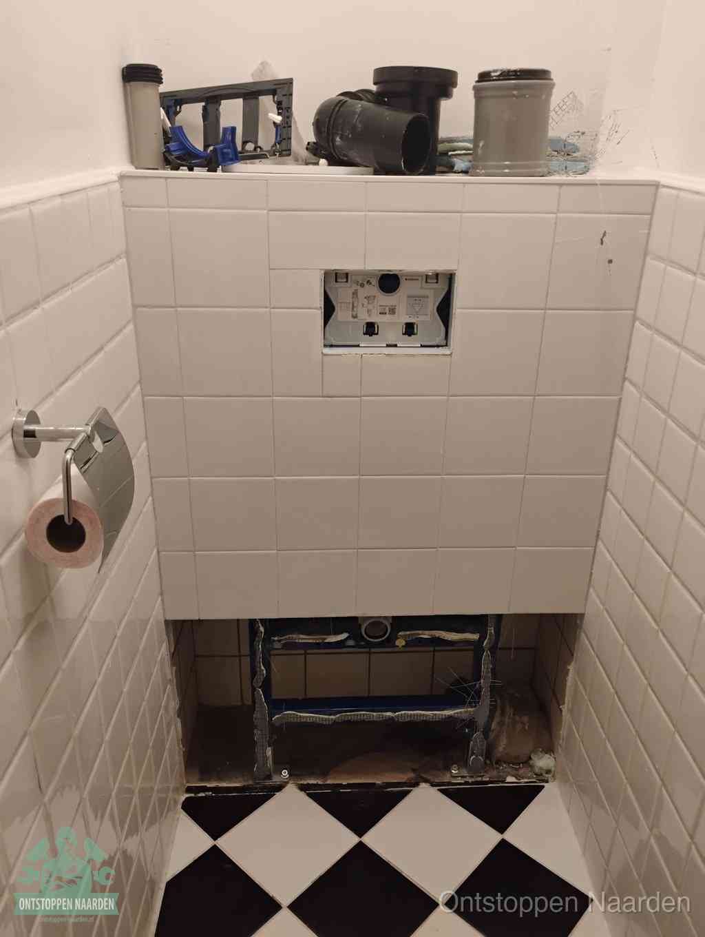 Een toiletruimte waar het hangtoilet en de inbouwreservoir-onderdelen zijn vrijgelegd voor onderhoud, periodiek nazicht voorkomt een wc-verstopping in Naarden