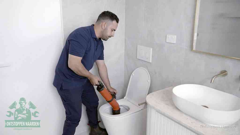 Een man gebruikt een handmatige luchtdruk-ontstopper in een modern betegeld toilet om zelf de wc te ontstoppen in Naarden